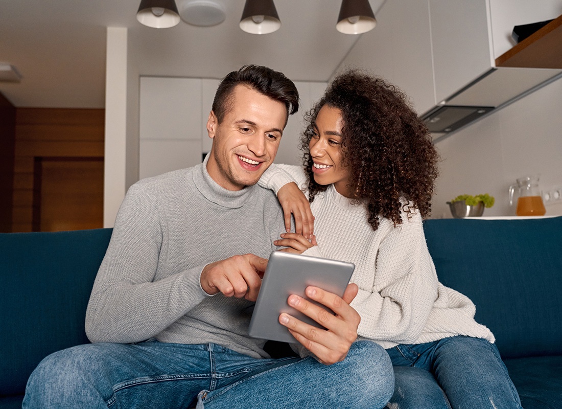 Romantic Date. Young multiethnic couple at home sitting on sofa browsing digital tablet together smiling cheerful